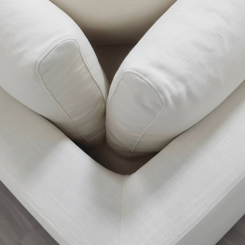 Close-up of the Snowdrift Sectional Sofa, a modular 2-piece arm unit in cream, featuring large cushions in its corner and highlighting the texture and stitching details of the premium fabric against a wooden floor.
