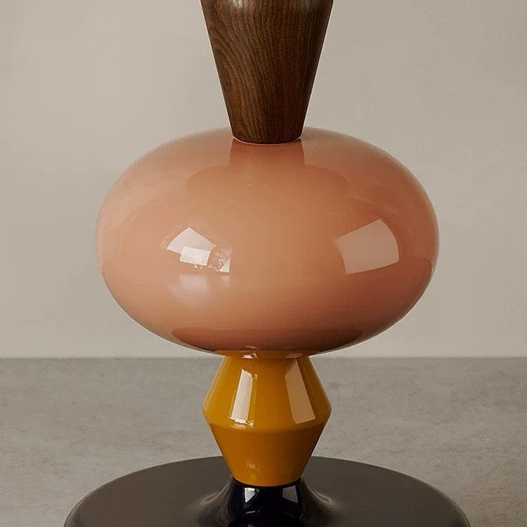 A close-up of the 糖葫芦茶几, a sculptural table with stacked geometric shapes in green, wood, pink, yellow, and black, displayed on a smooth surface against a neutral background.