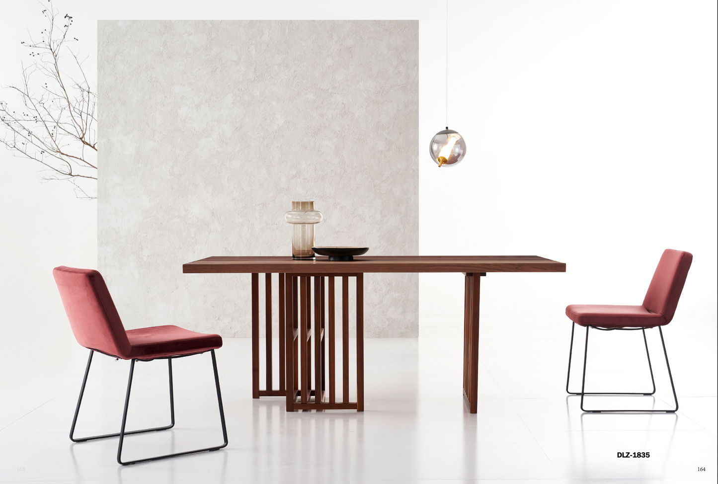 Solid Wood Dining Table adorned with two red chairs. A small branch in a vase and pendant light add charm to the textured wall backdrop.
