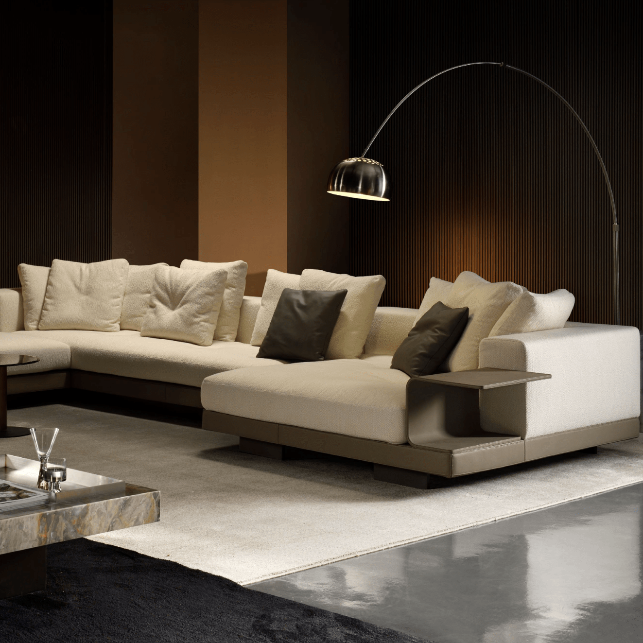 A modern living room showcases a beige sectional sofa with decorative cushions, illuminated by the Arch Floor Lamp featuring stainless steel and marble. The marble coffee table holds magazines and decor items, while soft ambient lighting enhances the dark walls' elegance.