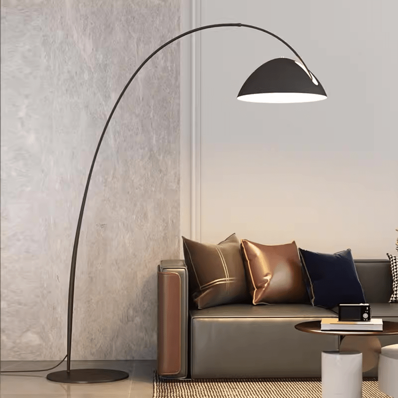 A minimalist living room features a Black Arch Floor Lamp with an arched neck next to a sofa adorned with assorted cushions.
