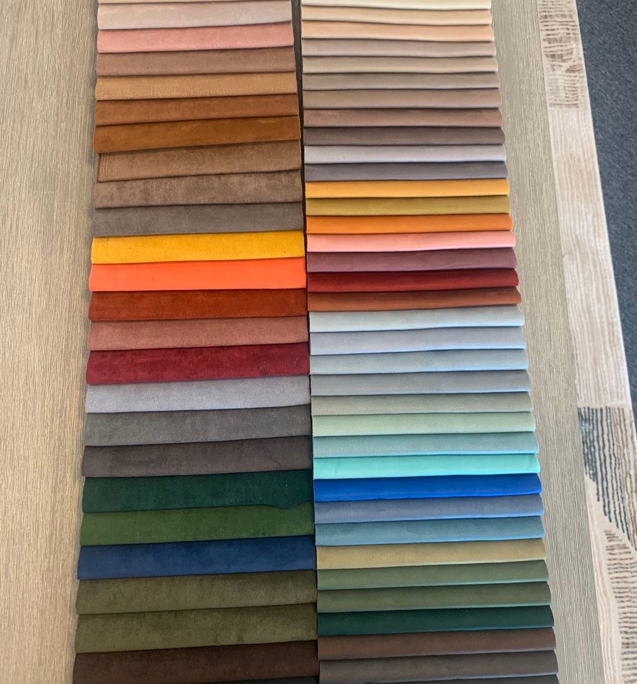 Fabric swatches in neutrals, reds, oranges, greens, and blues are laid out in a grid on a table—ideal for choosing the perfect hue for your Large Chillax Lounger – 3 Seat Sofa or enhancing your TOGO sofa lounging experience.