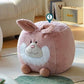 The Adorable Animal Ottoman Stool, available as a bunny or chicken, features a plush pink rabbit design with a smiling face and ears. It's perfect for whimsical decor in kids' bedrooms, resting on round feet atop a green rug and enhancing any cozy room setting.