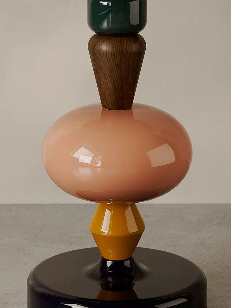 A close-up of the 糖葫芦茶几, a sculptural table with stacked geometric shapes in green, wood, pink, yellow, and black, displayed on a smooth surface against a neutral background.