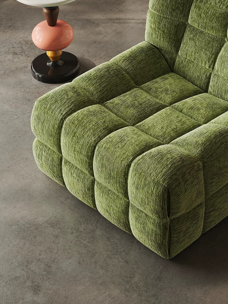 The 休闲椅2, a green tufted upholstered chair with a geometric pattern, sits beside a small round side table with a white top and pink base on a concrete floor.