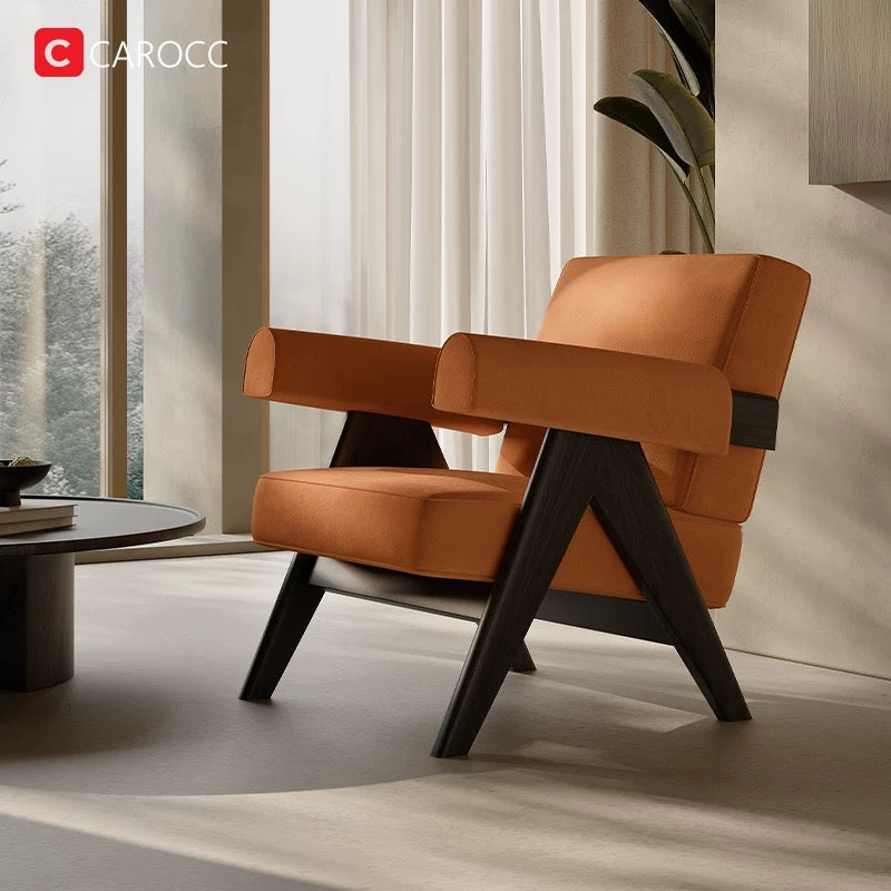 A 休闲椅 in a modern orange design with dark wooden legs is placed in a sunlit room beside a round coffee table and large window with white curtains.