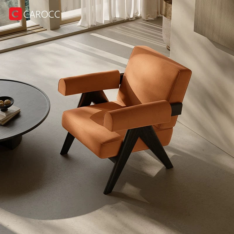 A 休闲椅 with a modern orange design and black wooden legs and arms is placed near a round coffee table in a sunlit room.