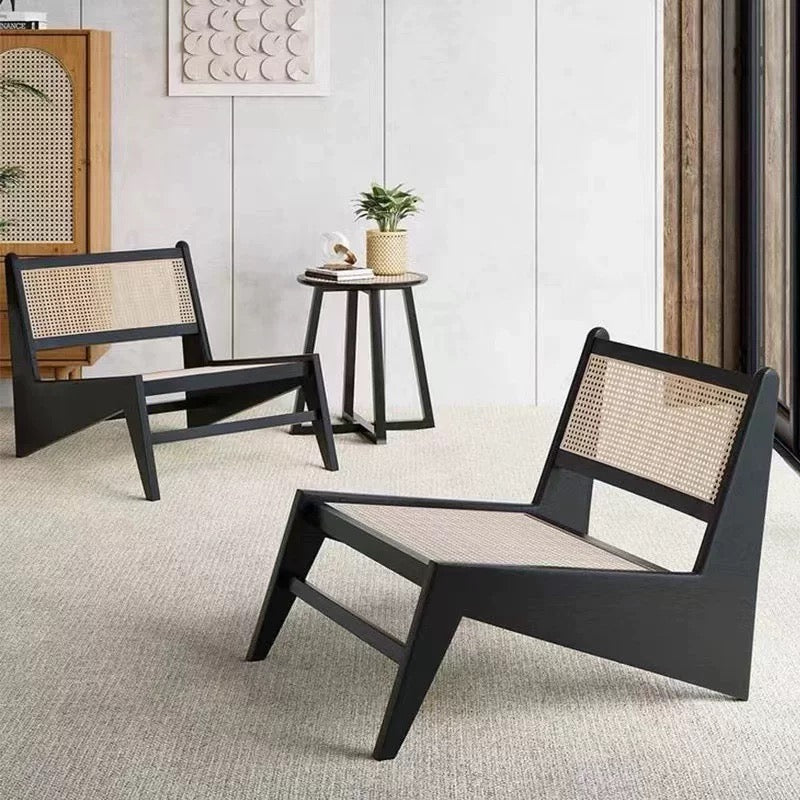 Two modern black 袋鼠椅 with woven rattan seats and backs sit on a light carpet, with a small round table holding a potted plant between them.