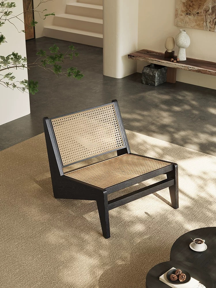 The 袋鼠椅, a modern low chair with a woven cane seat and backrest, stands on a beige carpet in a minimalist living room with neutral decor.