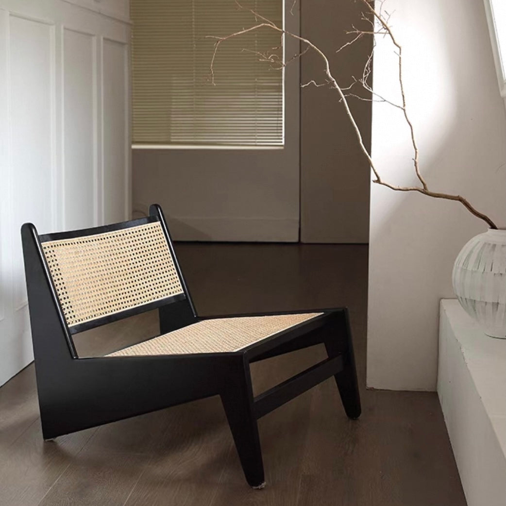 The 袋鼠椅, a modern black chair with a woven cane seat and backrest, sits on a wooden floor beside a window and a white vase filled with bare branches.