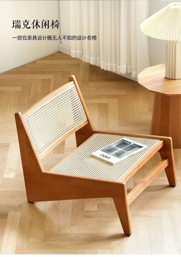 The 袋鼠椅, a wooden lounge chair with a woven cane seat and backrest, sits on a light wood floor beside a small table topped with a lamp and magazine.