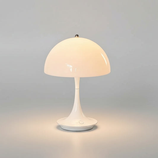 The Cordless Mashroom Lamp, a small modern white mushroom-shaped rechargeable table lamp, is lit on a countertop next to a framed print and a coffee machine.
