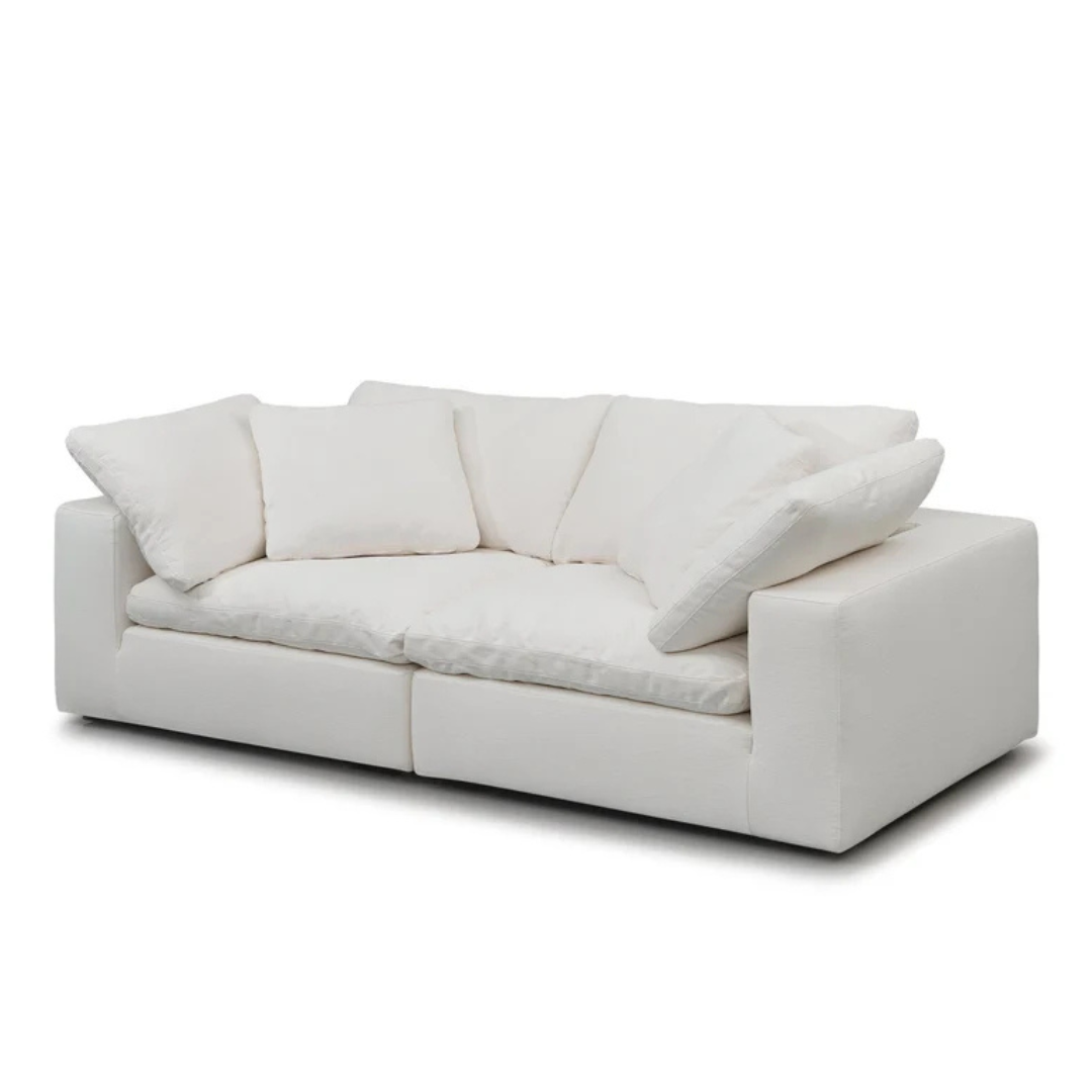 The Heavenly Sectional Sofa is a cream white modular 2-piece set crafted from ultra-soft materials, featuring two wide cushions and four matching pillows, all with washable covers, set against a plain background.