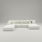 A modern sectional sofa in off-white upholstery with a chaise lounge on the left, several matching accent pillows, and two patterned throw pillows, shown on a plain white background.